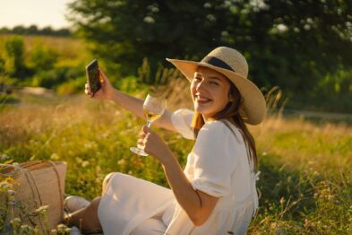 Girl with a glass of champagne or white wine makes a selfie on the phone. People using technology.