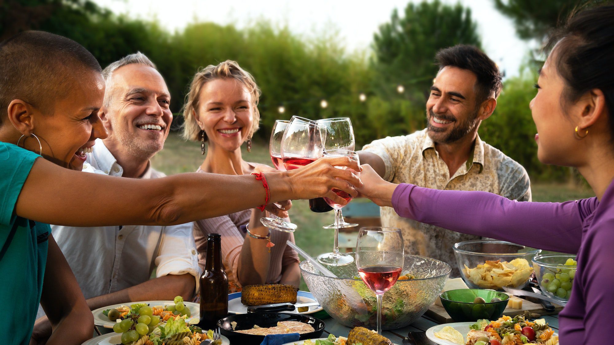 Happy friends toasting with wine during barbecue garden dinner party in the evening. Lifestyle.